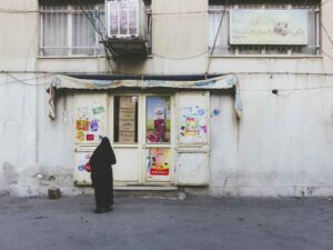 Une femme de dos lit les inscriptions sur la porte d'une épicerie de Téhéran. Des photographies de voyage originales, sincères et esthétiques qui subliment vos destinations.