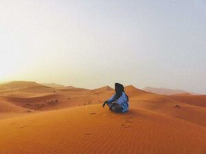 Un bédouin assis au milieu des dunes du désert du Sahara. Des photographies de voyage originales, sincères et esthétiques qui subliment vos destinations.