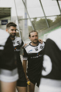 Des joueurs en groupe écoutent l'entraineur qui parle, près du terrain de sport. GAA Des photographies sportives pour révéler l'émotion et la beauté du geste.